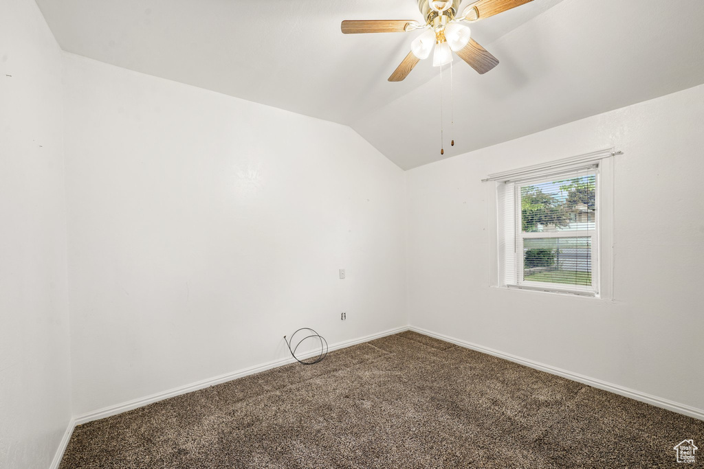 Empty room featuring carpet flooring, baseboards, vaulted ceiling, and a ceiling fan