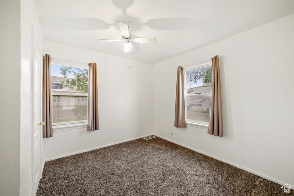 Empty room featuring plenty of natural light, dark colored carpet, a ceiling fan, and baseboards