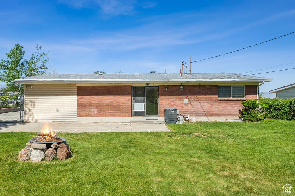 Rear view of house with an outdoor fire pit, brick siding, a patio, and a lawn