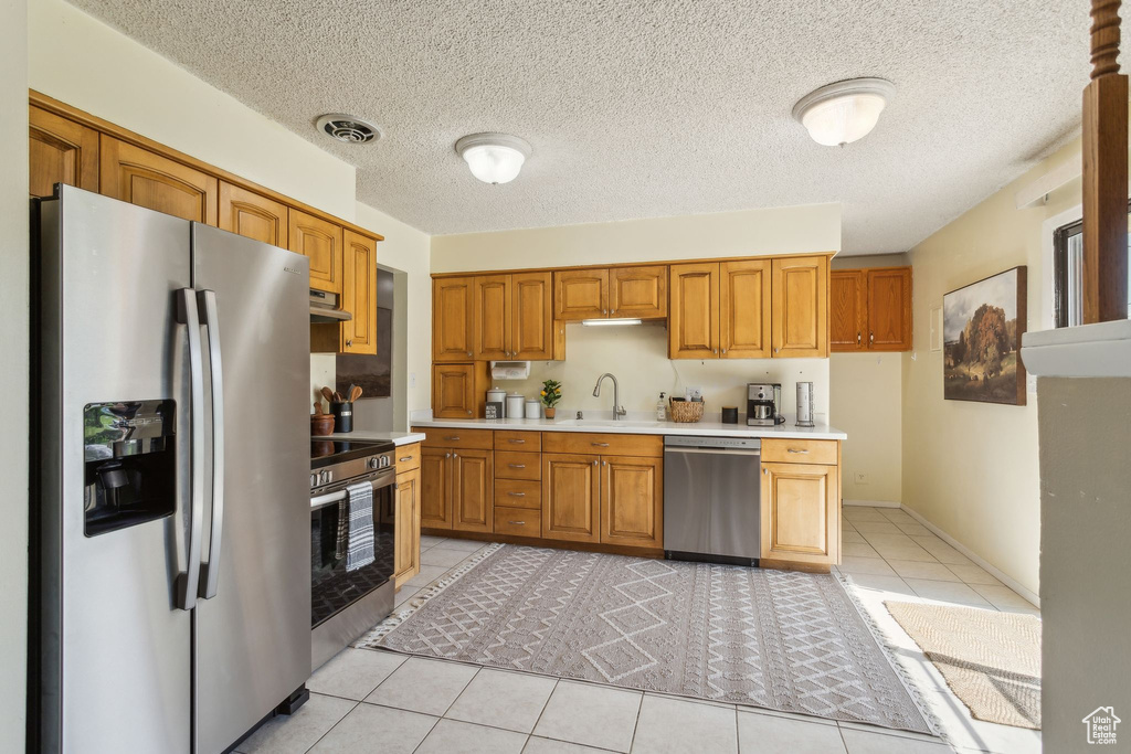 Kitchen with appliances with stainless steel finishes, light countertops, a sink, light tile patterned floors, and under cabinet range hood