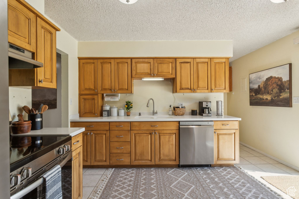 Kitchen featuring stainless steel appliances, a sink, under cabinet range hood, light countertops, and light tile patterned floors