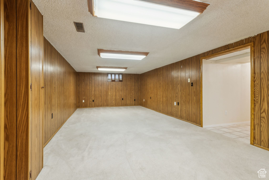 Finished below grade area featuring a textured ceiling, light carpet, and wooden walls