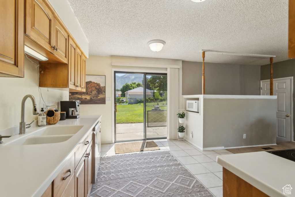 Kitchen featuring a sink, light countertops, light tile patterned floors, stainless steel dishwasher, and a textured ceiling