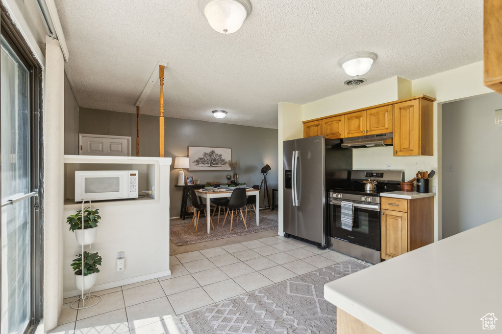 Kitchen with stainless steel appliances, under cabinet range hood, light countertops, light tile patterned flooring, and a textured ceiling