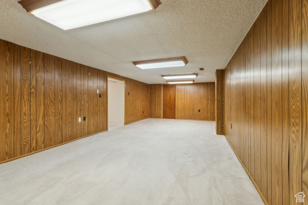 Unfurnished room featuring wood walls, a textured ceiling, and light colored carpet