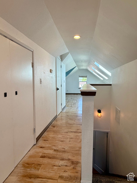 Hallway with light wood-style floors and vaulted ceiling