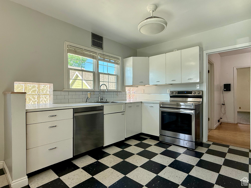 Kitchen with stainless steel appliances, dark flooring, light countertops, a sink, and white cabinets