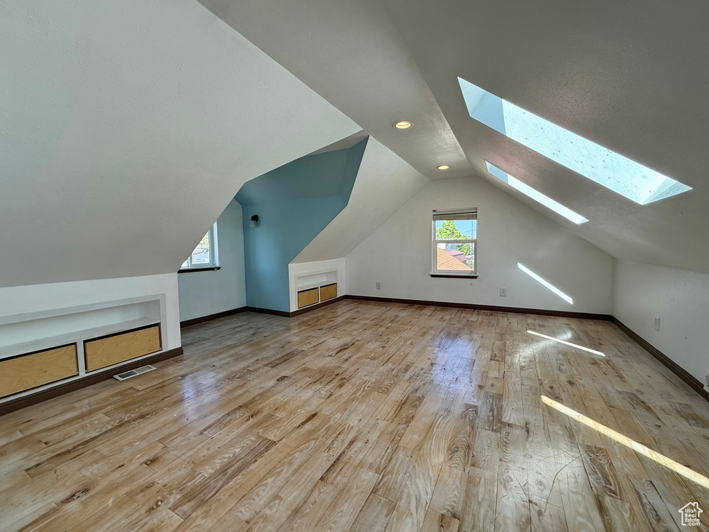 Bonus room with a skylight, hardwood / wood-style flooring, lofted ceiling, and baseboards