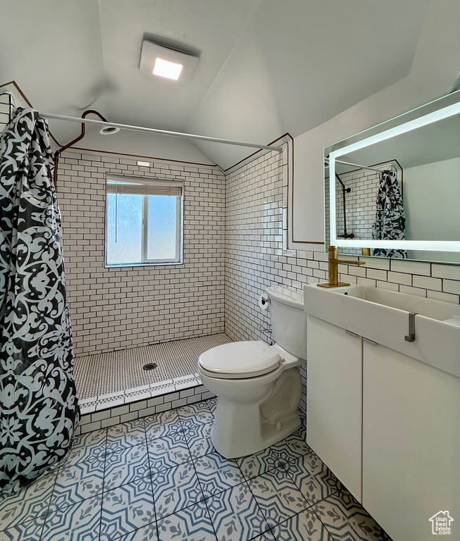 Bathroom with toilet, tile patterned floors, a tile shower, tile walls, and vaulted ceiling