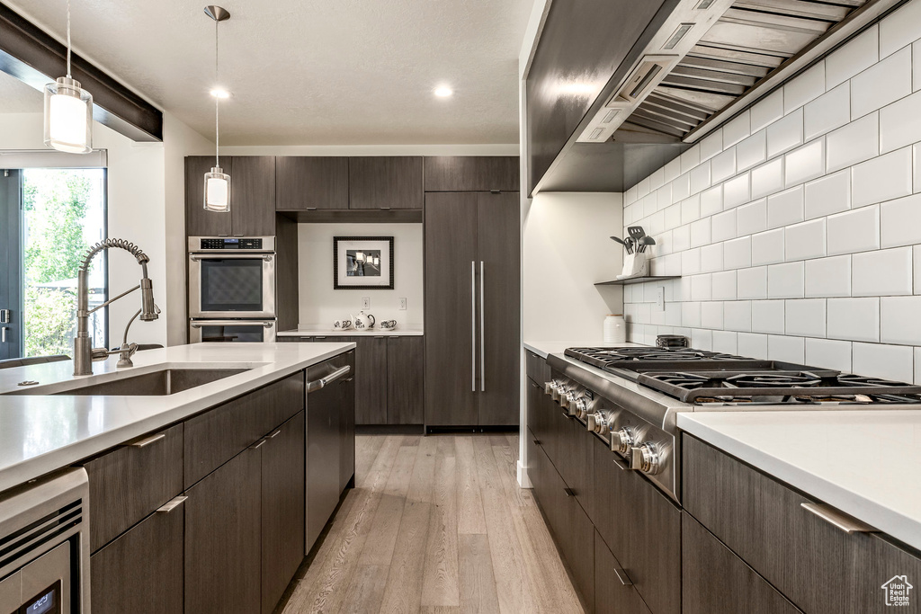 Kitchen with a sink, wall chimney exhaust hood, appliances with stainless steel finishes, light wood-style flooring, and dark brown cabinets