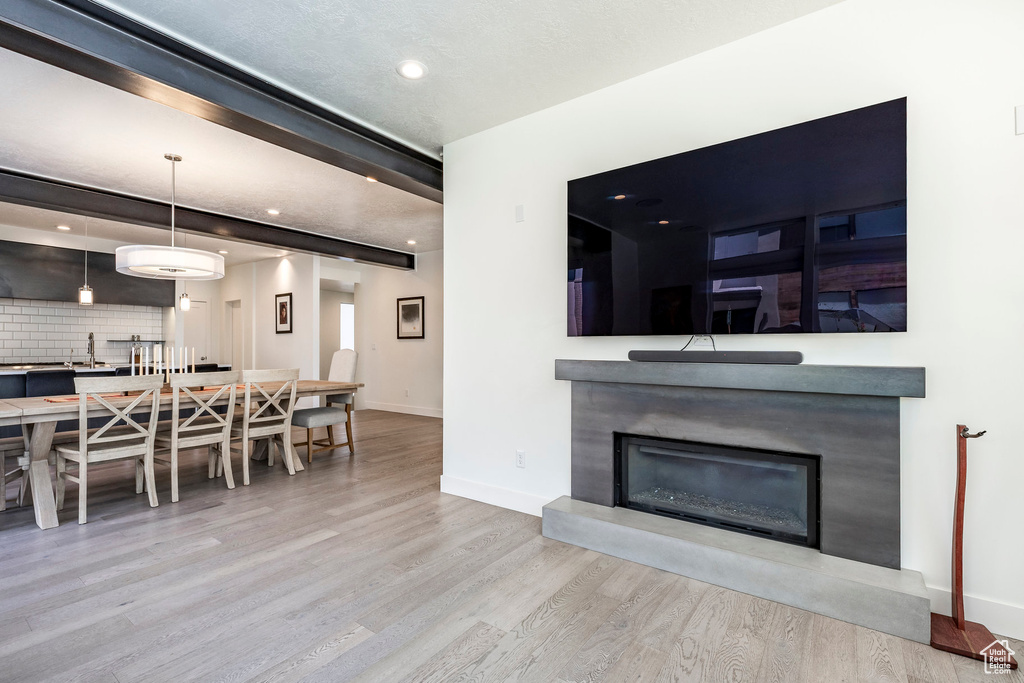 Living area with wood finished floors, a glass covered fireplace, baseboards, recessed lighting, and beamed ceiling