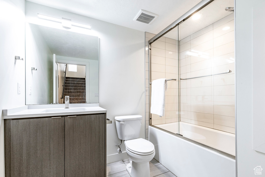 Bathroom with toilet, vanity, bath / shower combo with glass door, and baseboards