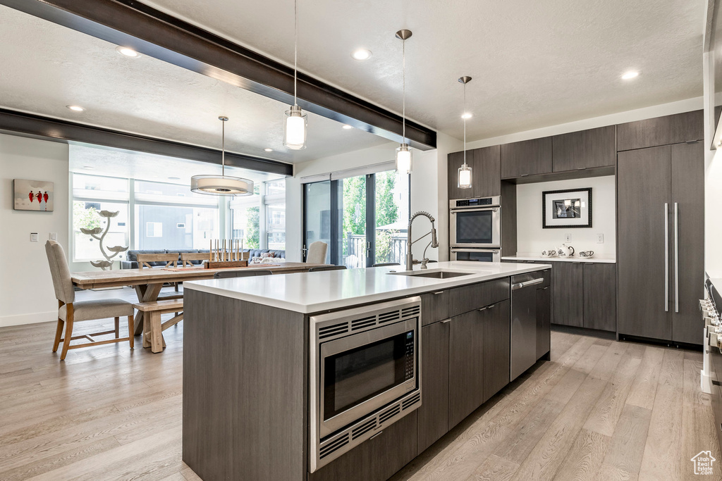 Kitchen featuring a sink, appliances with stainless steel finishes, an island with sink, light countertops, and light wood-type flooring