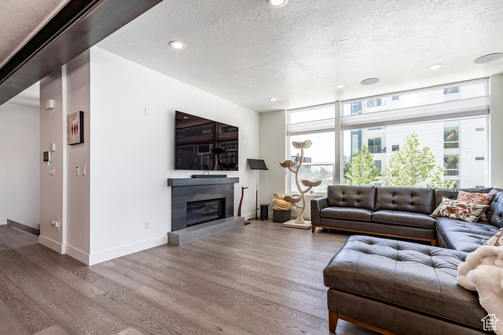 Living area featuring a textured ceiling, wood finished floors, baseboards, a glass covered fireplace, and recessed lighting