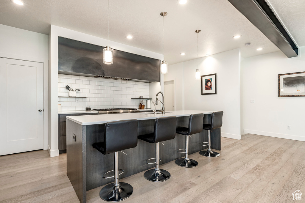 Kitchen with a sink, light wood finished floors, tasteful backsplash, light countertops, and recessed lighting