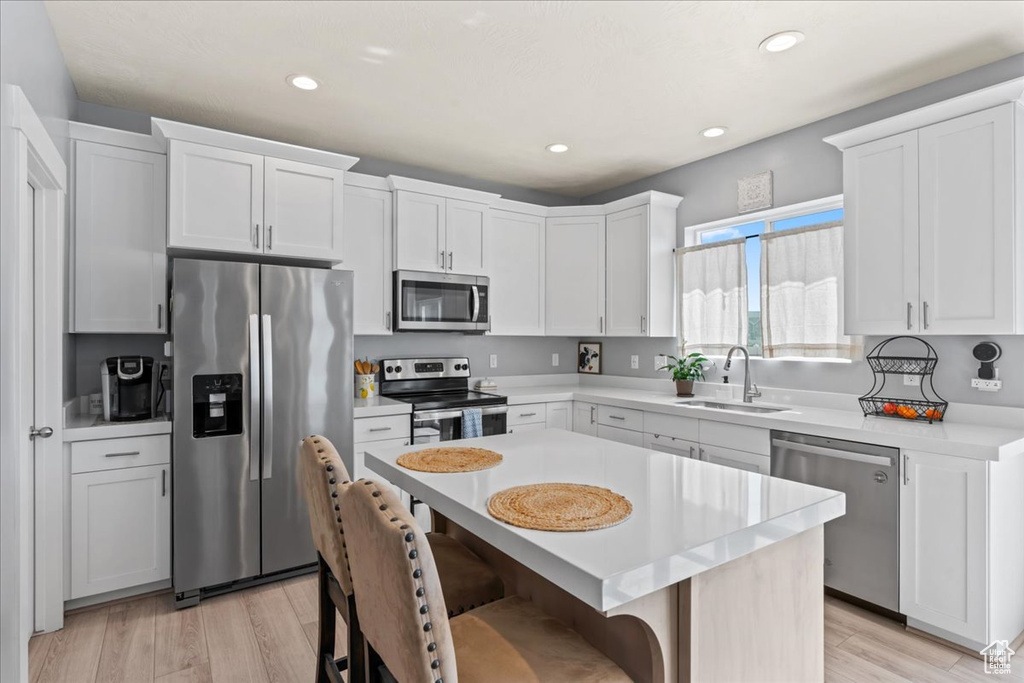 Kitchen with stainless steel appliances, a sink, a breakfast bar, light countertops, and light wood-style floors