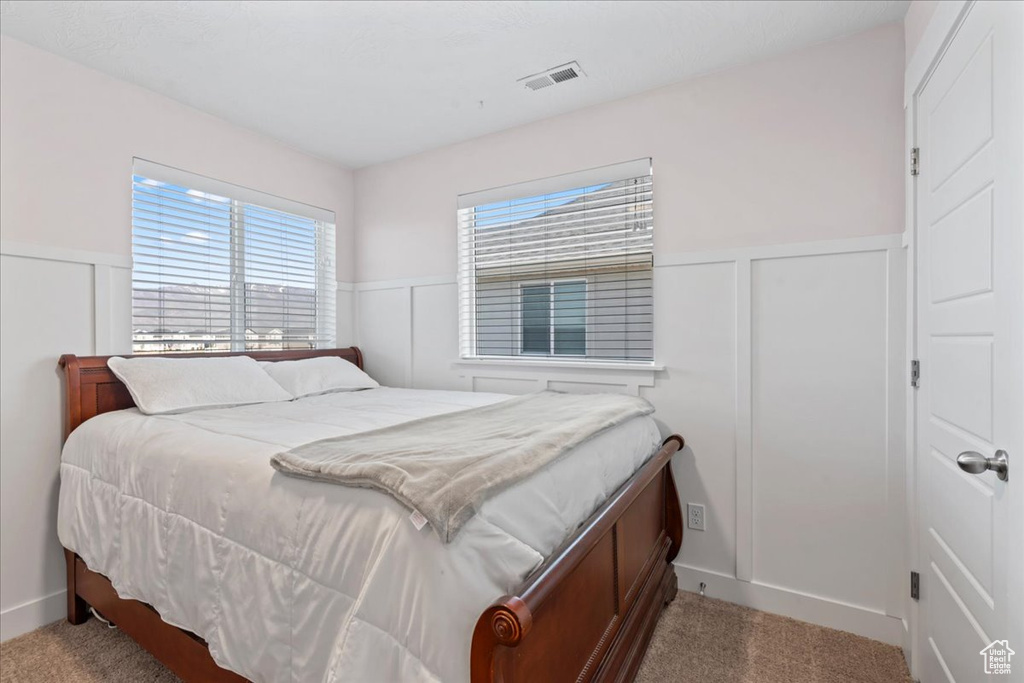 Carpeted bedroom featuring a wainscoted wall and a decorative wall
