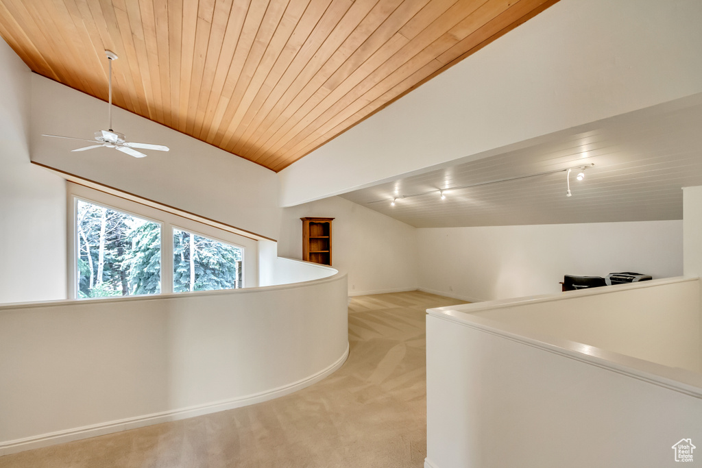 Corridor with vaulted ceiling, light colored carpet, wood ceiling, and baseboards
