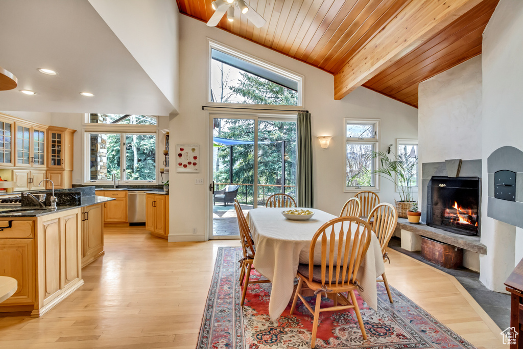 Dining area featuring a warm lit fireplace, plenty of natural light, light wood-style flooring, wooden ceiling with exposed beams, and recessed lighting