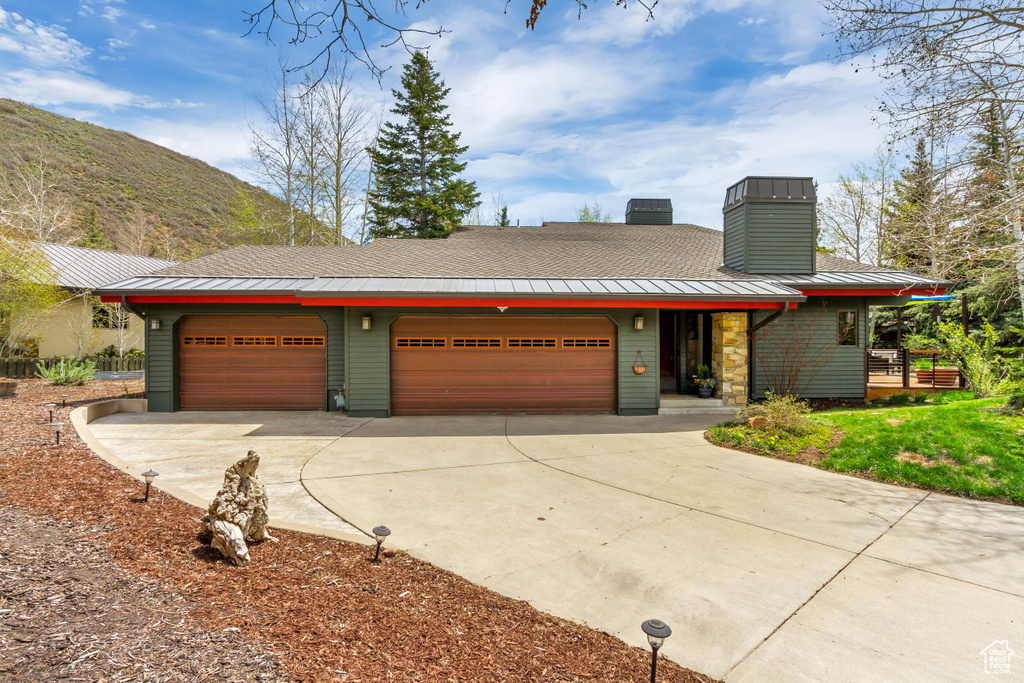 View of front of home with a standing seam roof, driveway, a chimney, an attached garage, and metal roof