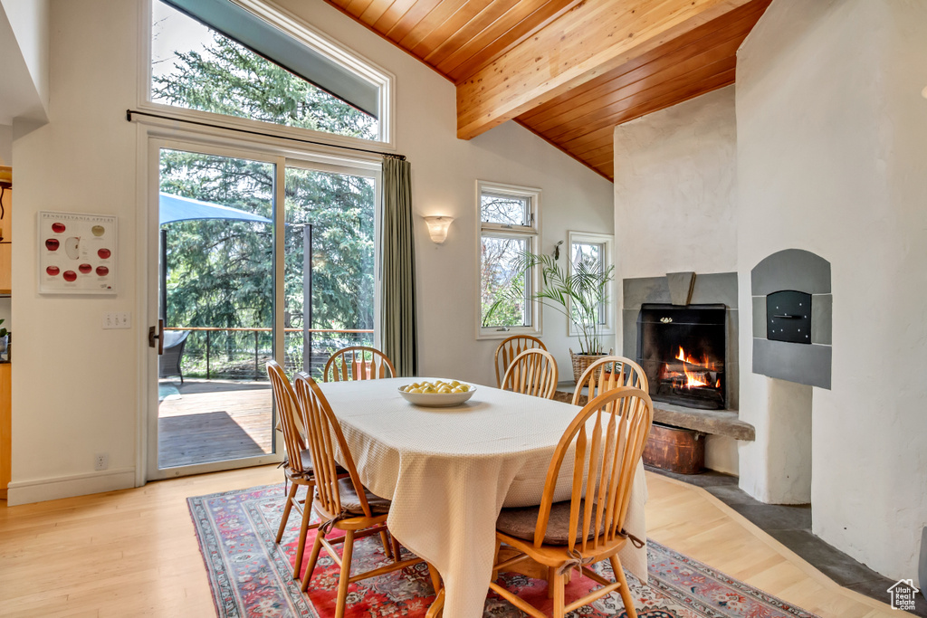 Dining room featuring wood ceiling with exposed beams, a lit fireplace, light wood-style flooring, and high vaulted ceiling
