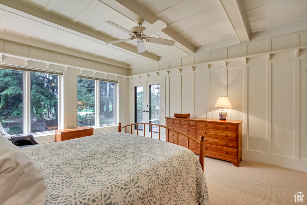 Bedroom featuring light colored carpet, multiple windows, beamed ceiling, a decorative wall, and access to exterior