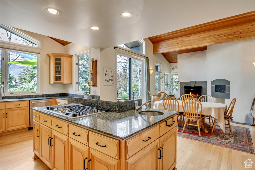 Kitchen with stainless steel appliances, a warm lit fireplace, light wood-style flooring, light brown cabinetry, and recessed lighting