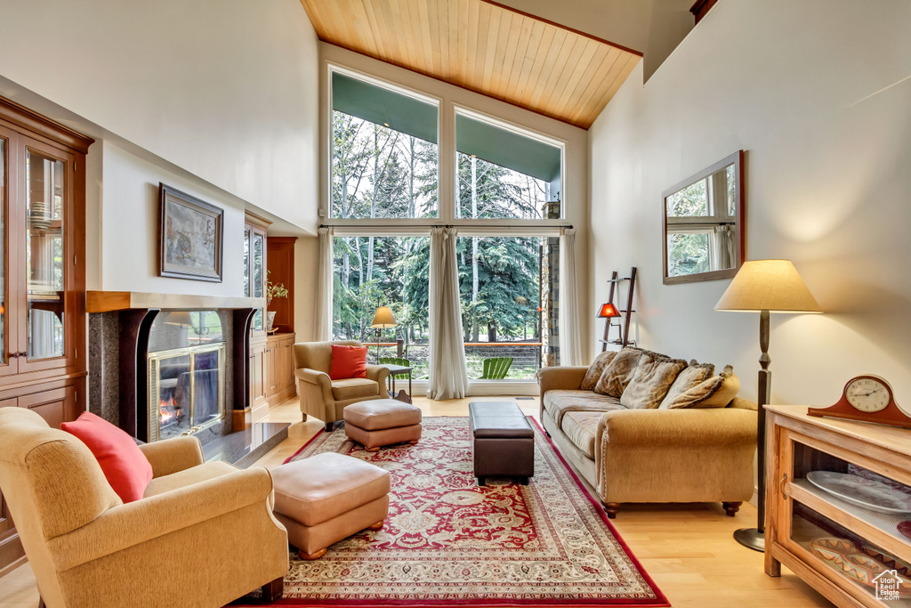 Living room featuring high vaulted ceiling, a high end fireplace, wood ceiling, light wood-style floors, and healthy amount of natural light