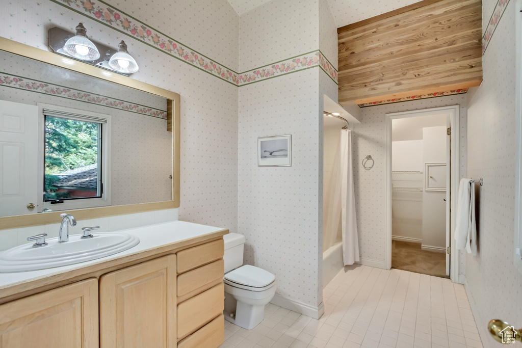 Full bathroom featuring vanity, toilet, wallpapered walls, shower / bathtub combination with curtain, and tile patterned flooring