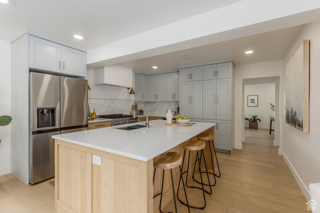 Kitchen with stainless steel fridge with ice dispenser, a sink, light wood-style flooring, tasteful backsplash, and a kitchen breakfast bar