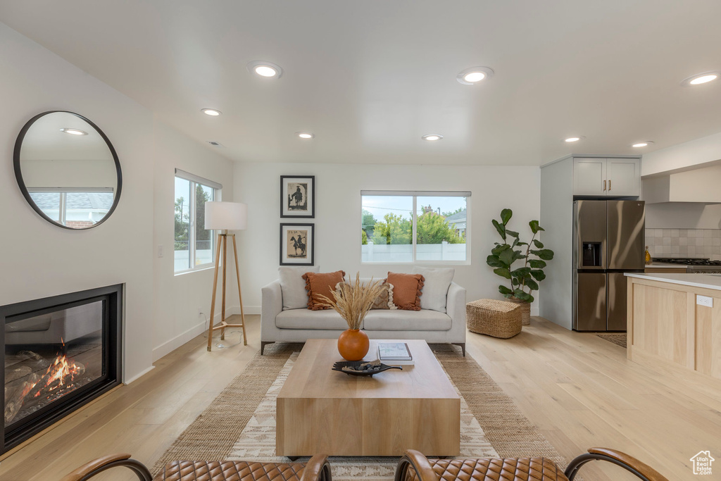 Living room with light wood-type flooring, recessed lighting, a glass covered fireplace, and baseboards