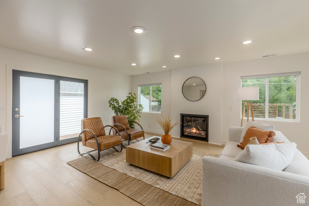 Living room featuring light wood-style floors, a glass covered fireplace, and recessed lighting