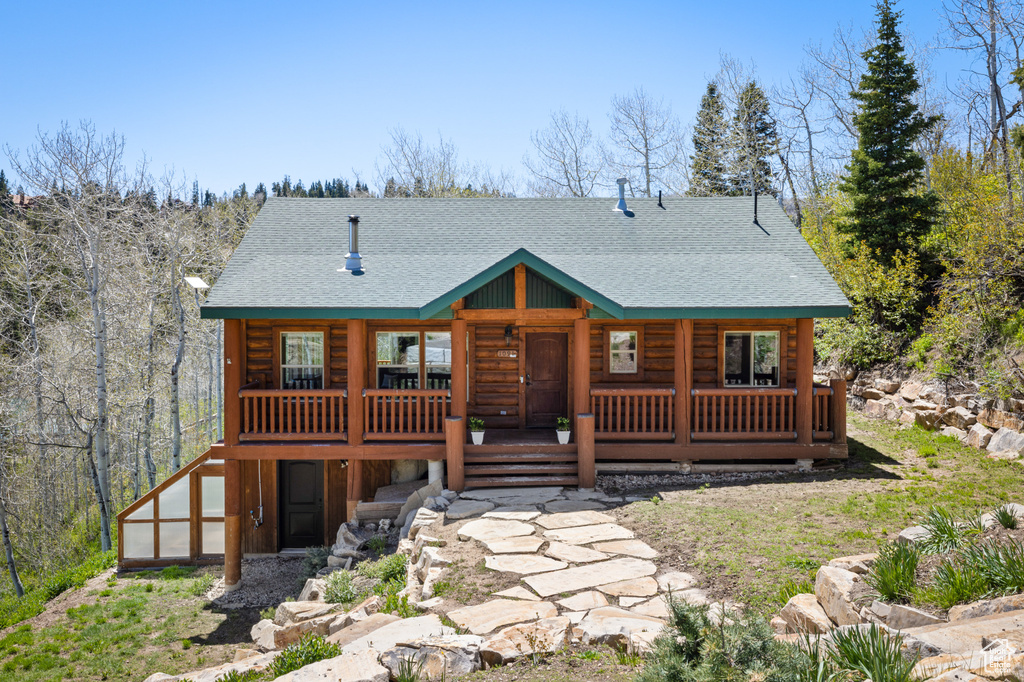 Log-style house featuring a shingled roof and a porch