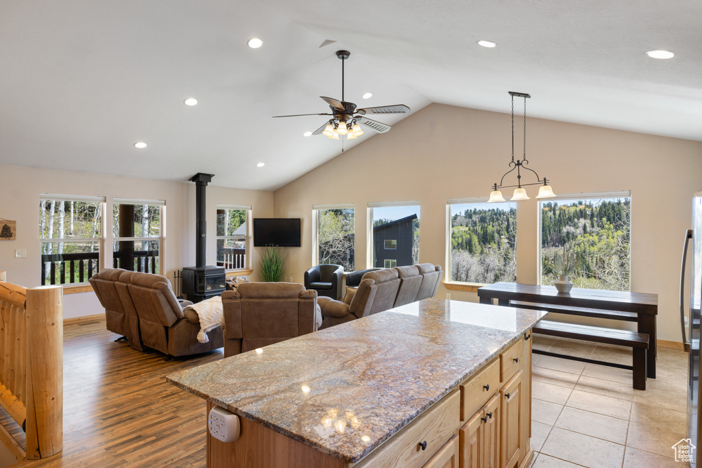 Kitchen featuring a wood stove, recessed lighting, a ceiling fan, light stone countertops, and a center island
