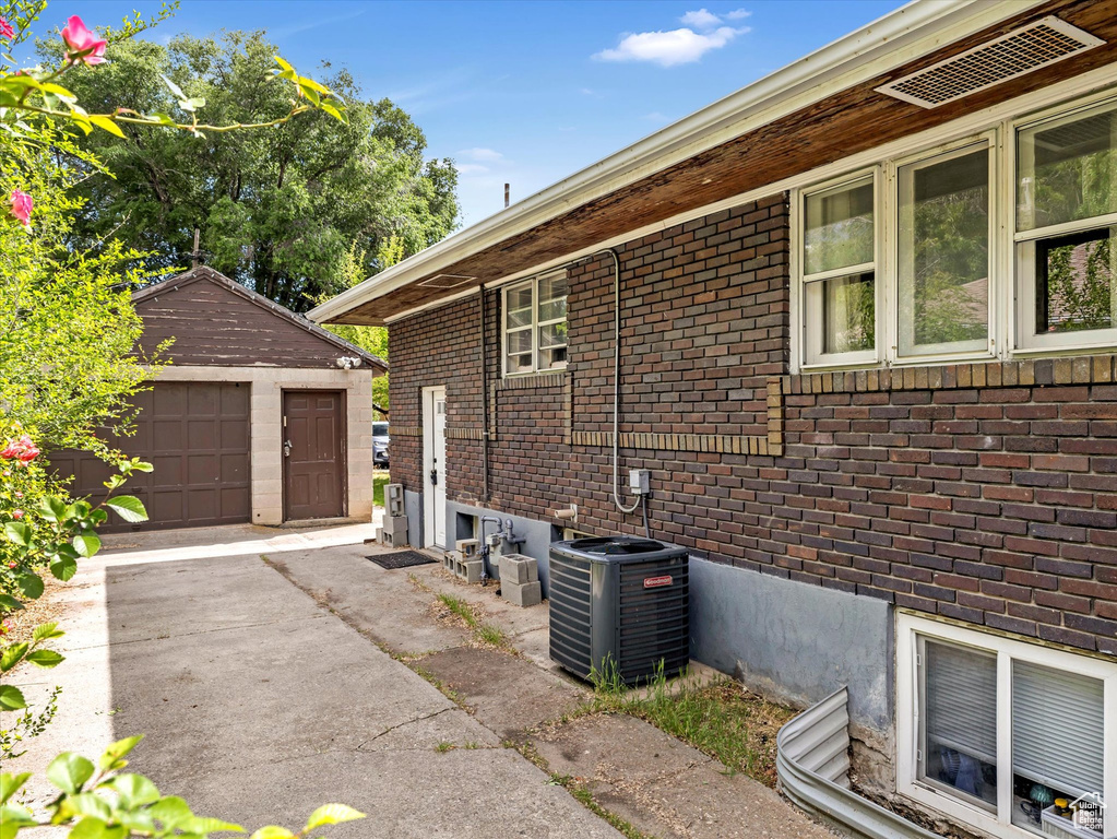 View of side of property with central air condition unit, brick siding, an outbuilding, and a garage