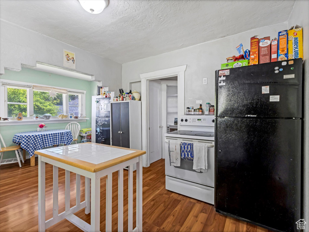 Kitchen with freestanding refrigerator, electric range, wood finished floors, and a textured ceiling