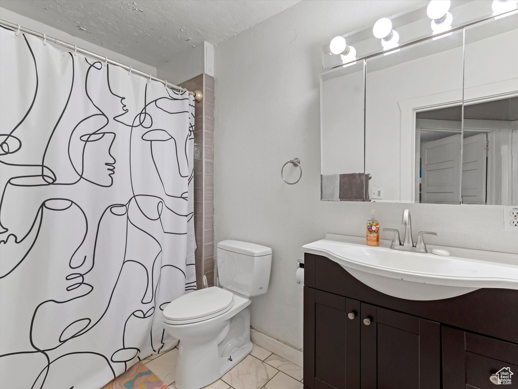 Bathroom featuring vanity, toilet, a textured ceiling, marble look tiles, and baseboards