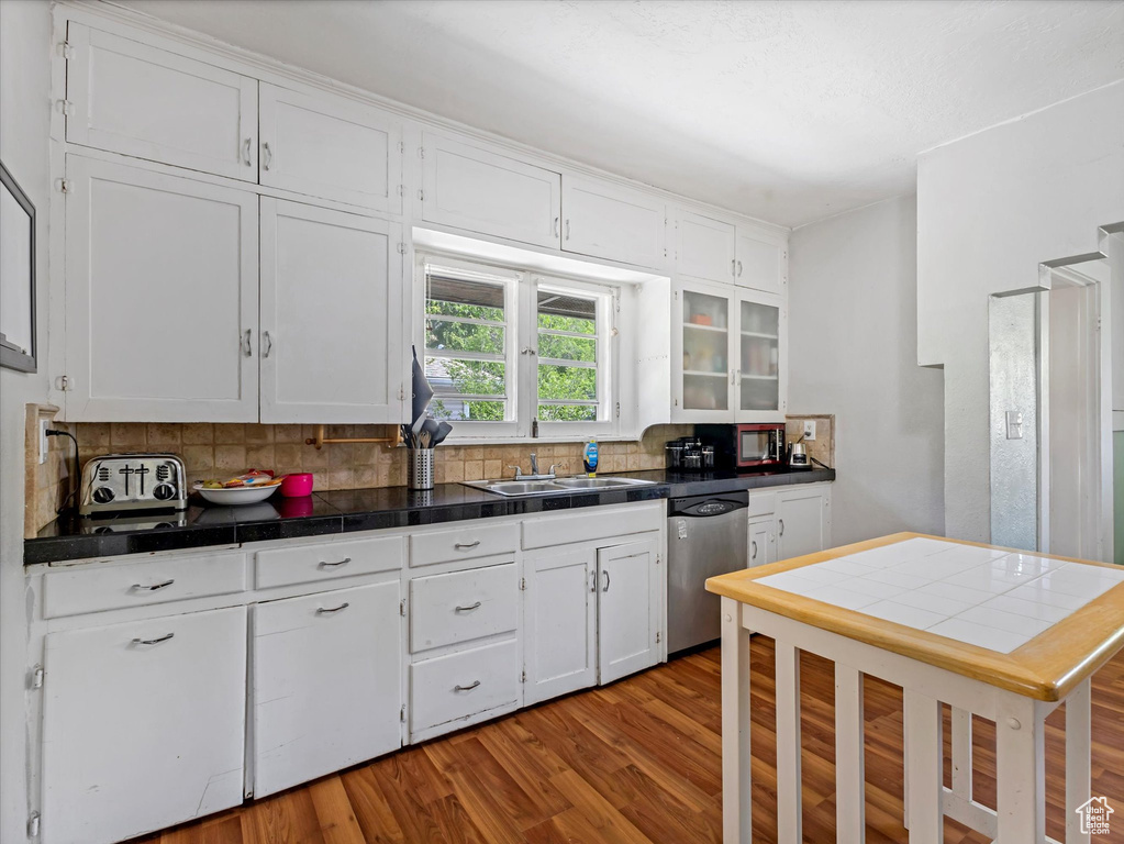 Kitchen featuring stainless steel dishwasher, a sink, white cabinets, and backsplash