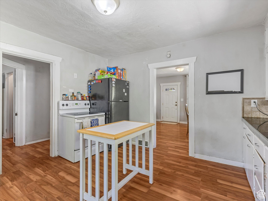 Kitchen with white range with electric cooktop, freestanding refrigerator, light wood finished floors, and baseboards