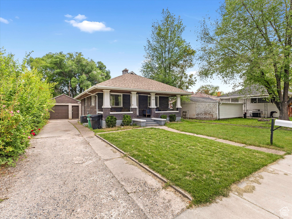 View of front of home with an outdoor structure, a detached garage, brick siding, a chimney, and a front lawn
