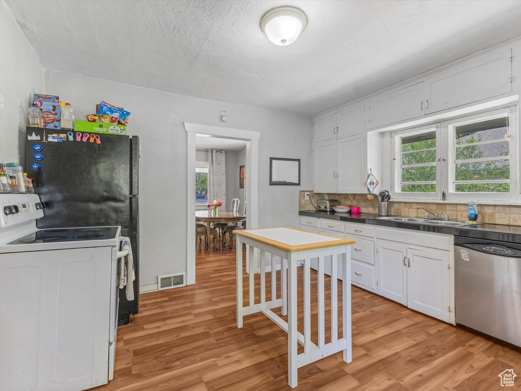 Kitchen with dishwasher, white electric range oven, a sink, light wood-type flooring, and dark countertops