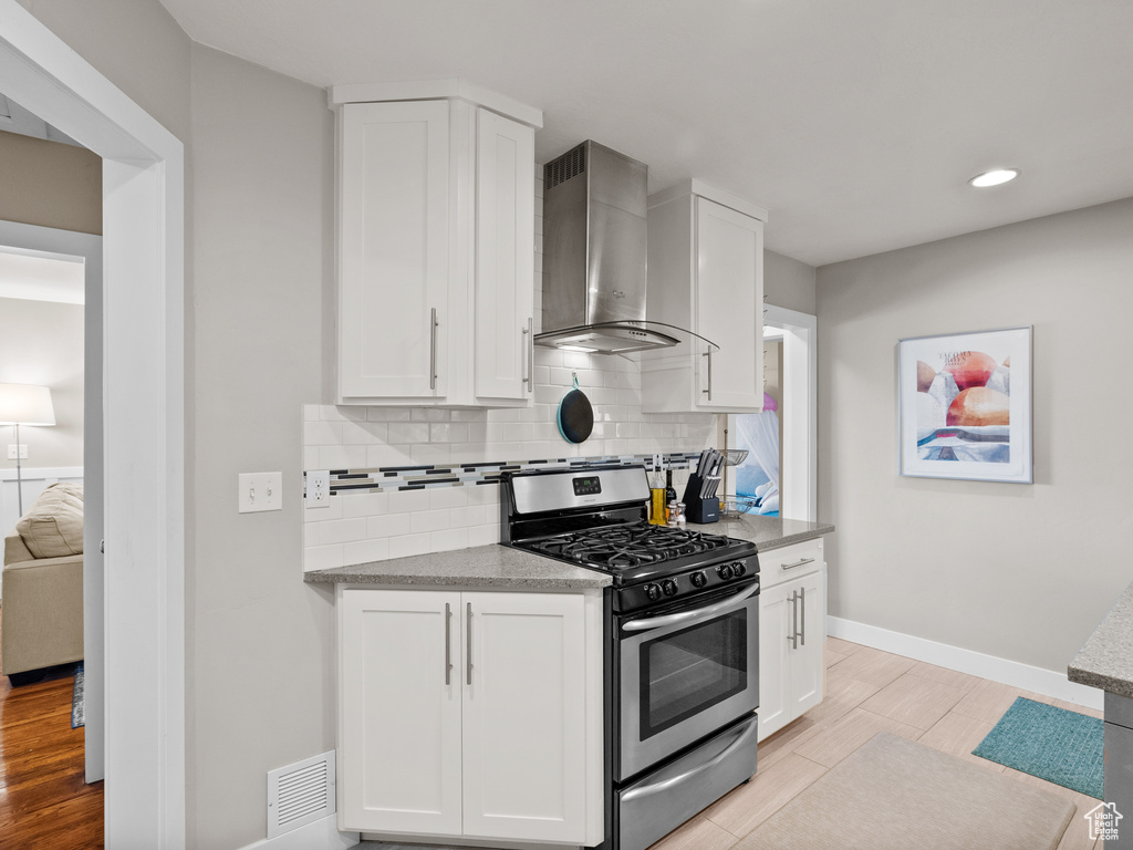 Kitchen with stainless steel gas stove, wall chimney range hood, backsplash, light wood finished floors, and recessed lighting