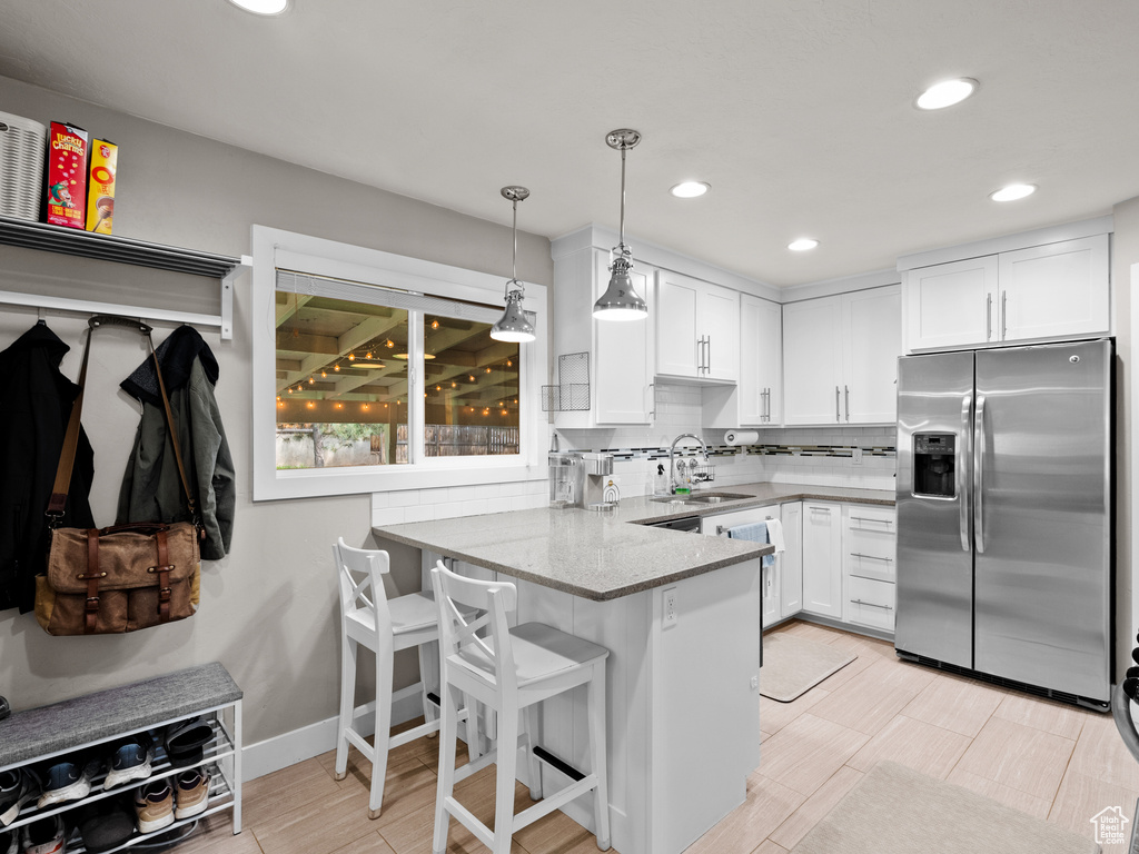 Kitchen with stainless steel refrigerator with ice dispenser, a sink, a peninsula, white cabinets, and decorative light fixtures