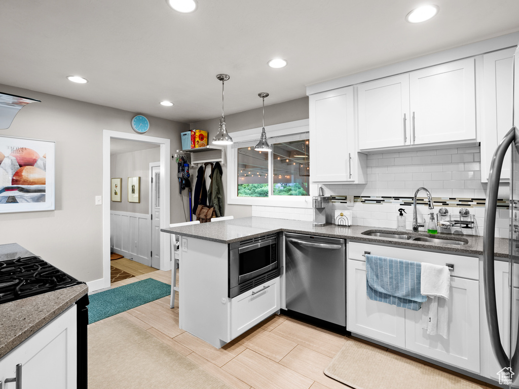 Kitchen with stainless steel appliances, a sink, white cabinetry, a peninsula, and backsplash