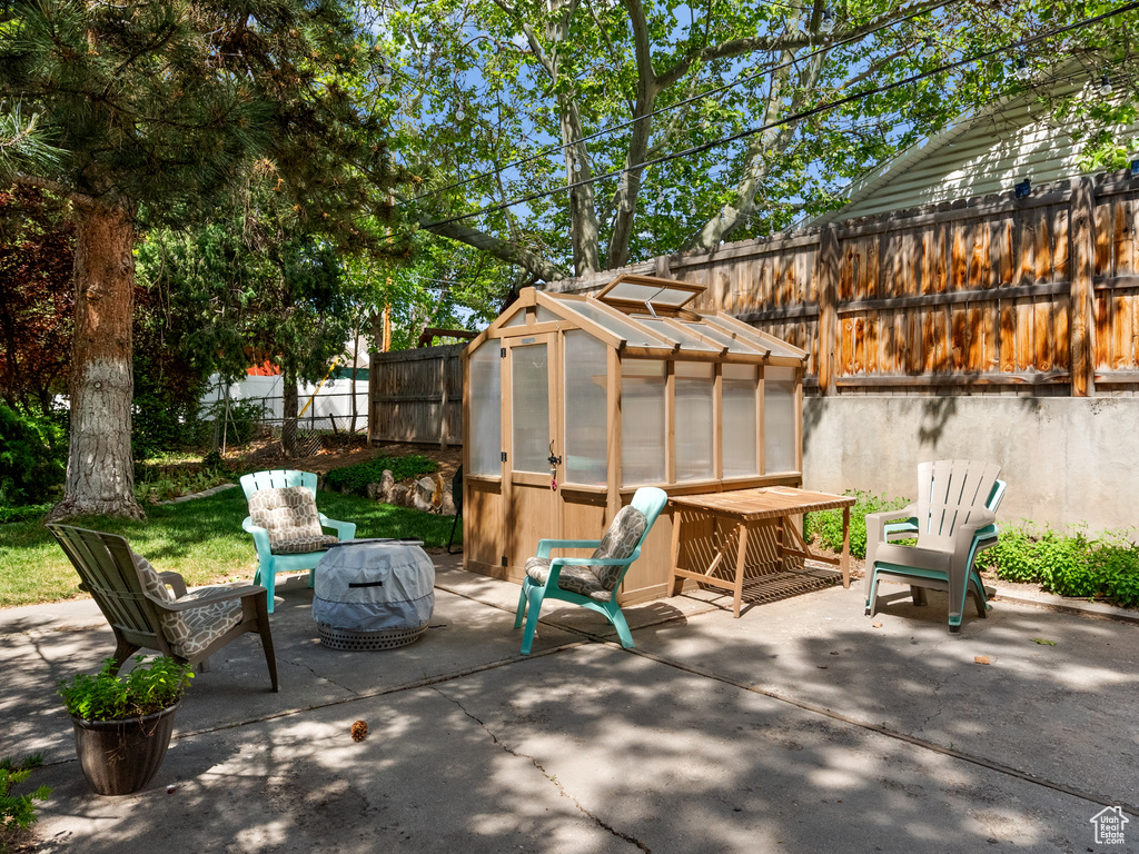 Fenced backyard with a greenhouse, an outdoor structure, and a patio area