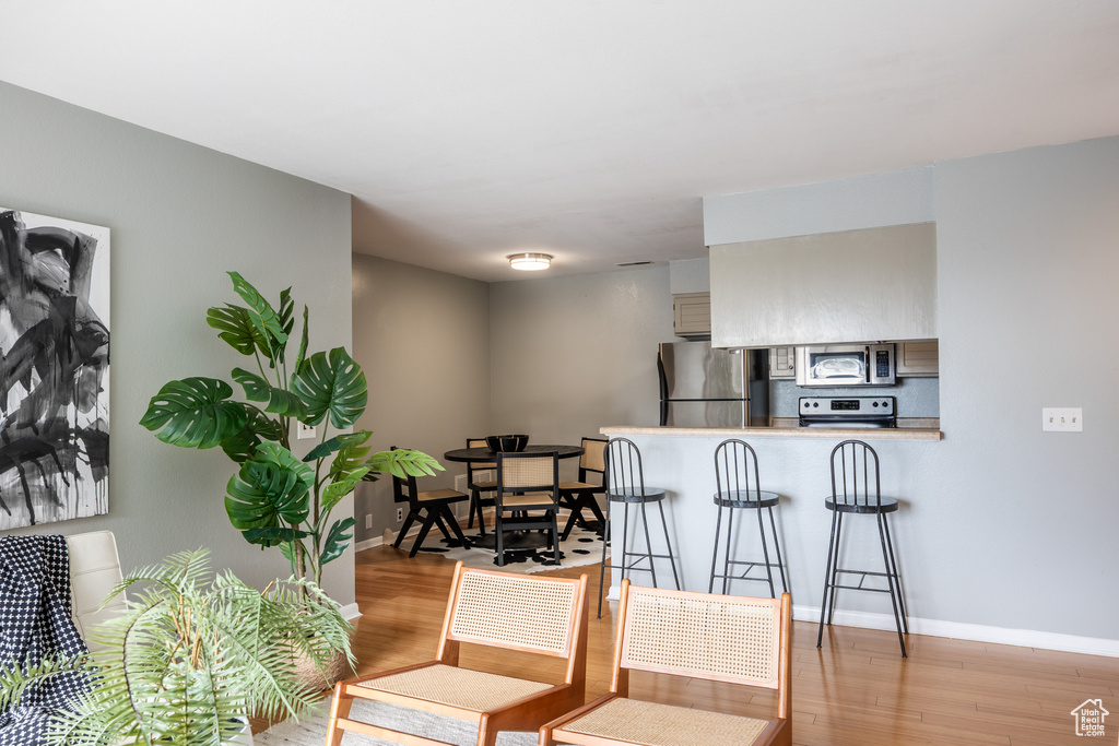 Kitchen with appliances with stainless steel finishes, light wood-style flooring, a peninsula, a kitchen bar, and baseboards