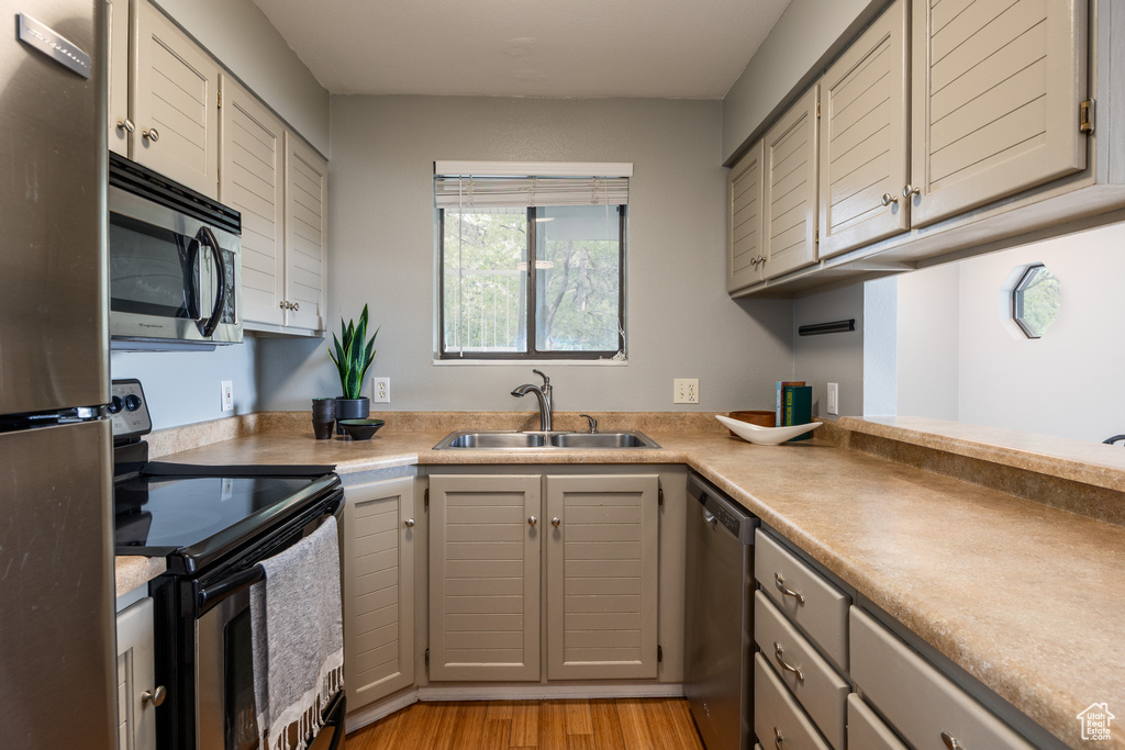Kitchen featuring stainless steel appliances, a sink, gray cabinetry, light wood-style floors, and light countertops