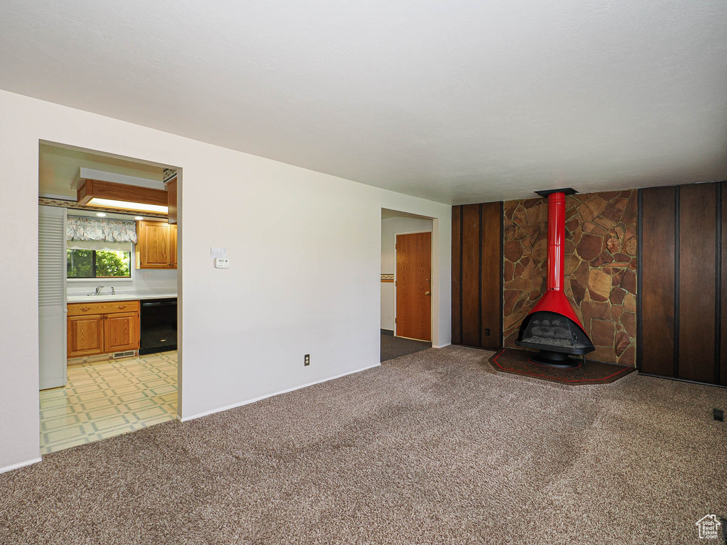 Unfurnished living room featuring a wood stove, a sink, light carpet, and baseboards