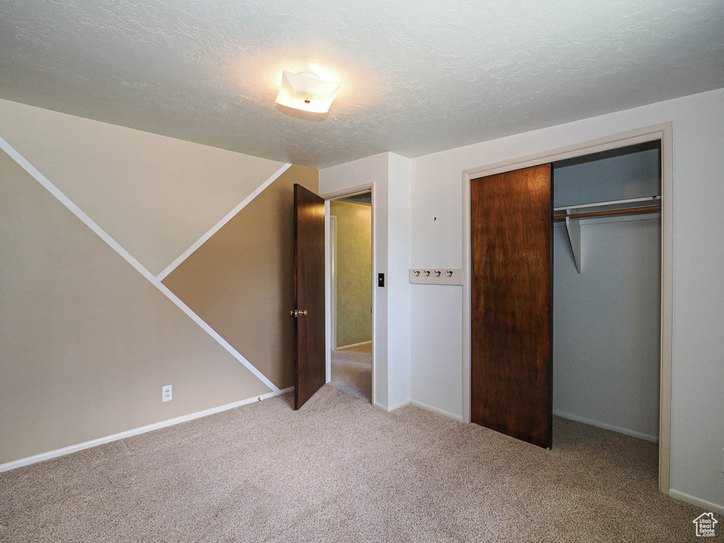 Unfurnished bedroom with carpet, baseboards, a closet, and a textured ceiling