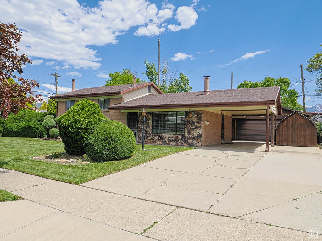 Tri-level home featuring a garage, driveway, a front lawn, and brick siding